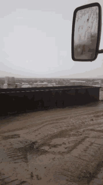 a dirty road with a reflection of a fence in a rear view mirror