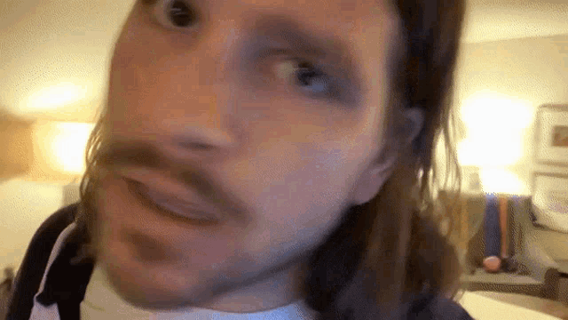 a man with long hair and a mustache is looking at the camera