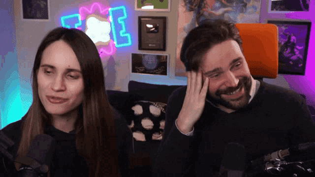 a man and a woman are laughing in front of a neon sign that says e