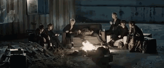 a group of people are sitting around a fire in a parking lot .