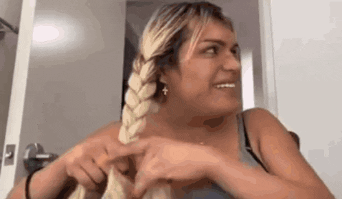 a woman is braiding her hair in a braid and making a face .