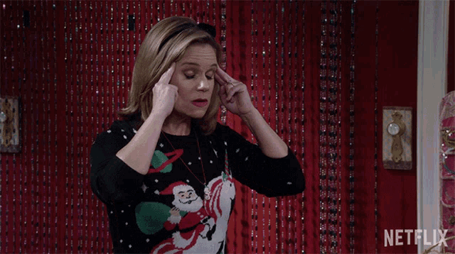 a woman wearing a christmas sweater with santa on it holds her head