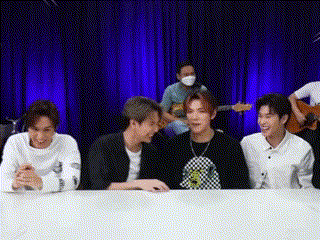 a group of young men are sitting at a table in front of a blue curtain and laughing .