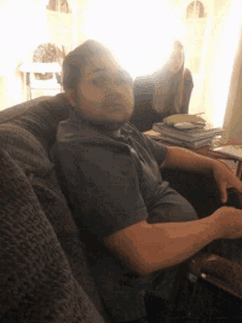 a man sits on a couch with a stack of books on a table behind him