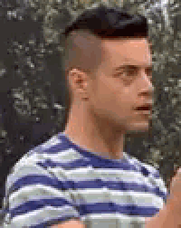 a man wearing a striped shirt and a mohawk is standing in a park .