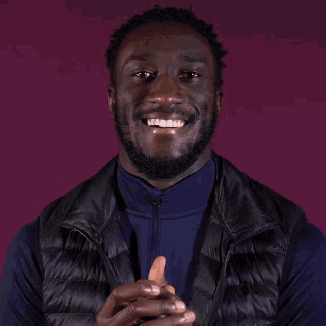 a man wearing a black vest is clapping his hands and smiling