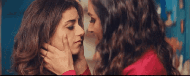two women are touching each other 's faces and one of them has a ring on her finger