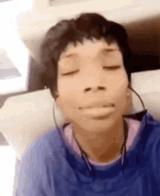 a young girl wearing headphones and a blue shirt is sitting on a chair with her eyes closed .