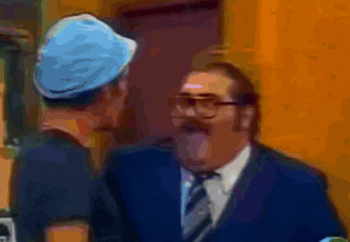 a man wearing glasses and a blue hat talks to another man