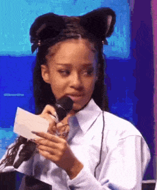 a girl with cat ears is holding a piece of paper in front of a microphone