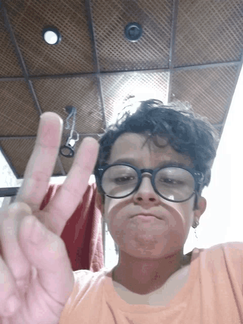 a young boy wearing glasses and earrings giving a peace sign