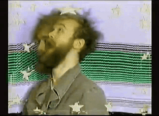a man with a beard is standing in front of a green and white striped blanket .