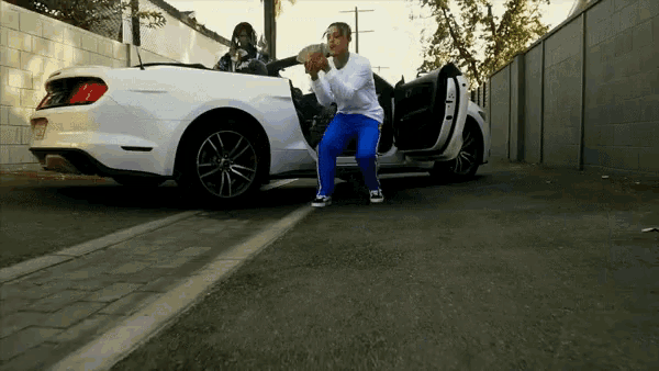 a man squatting in front of a white car with the door open