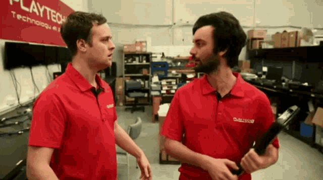 two men in red shirts are talking in front of a sign that says playtech
