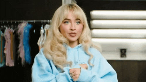 a blonde woman wearing a blue hoodie is standing in front of a row of clothes .