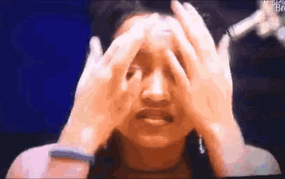 a woman is covering her face with her hands while looking at a microphone .