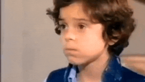 a young boy with curly hair is making a funny face in a close up of his face .