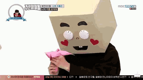 a man wearing a box on his head is holding a pink origami bird