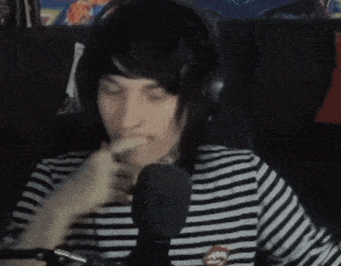 a man wearing headphones and a striped shirt is talking into a microphone with his eyes closed