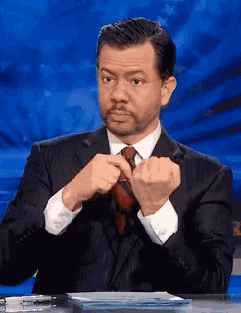 a man in a suit and tie adjusts his tie while sitting at a desk