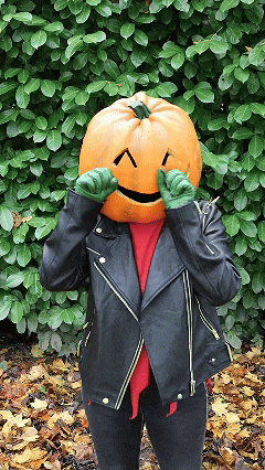 a person with a pumpkin head and green gloves covering their eyes