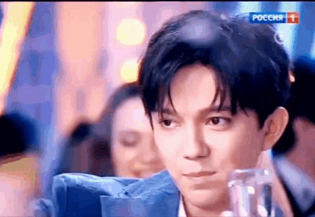 a man in a blue suit is holding a glass of water while looking at the camera .