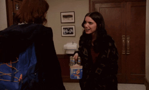 two women walking down a hallway with a red exit sign in the background