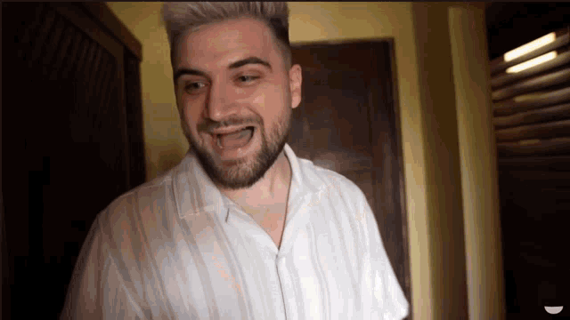 a man with a beard wearing a white shirt is smiling in a room .