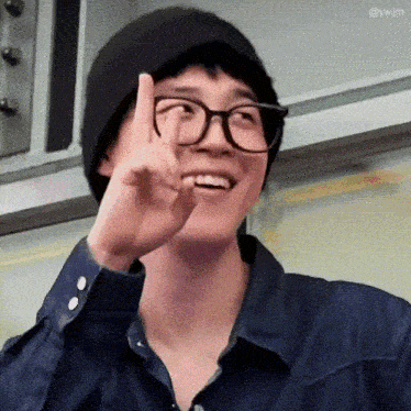 a man wearing glasses and a hat is giving the peace sign .