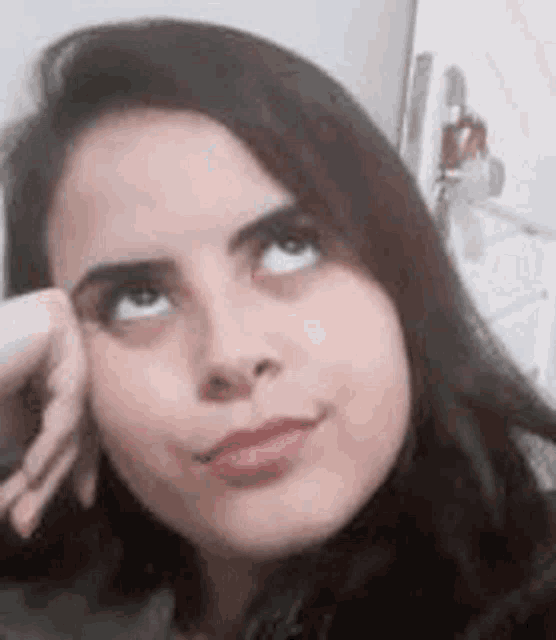 a close up of a woman 's face with her hand on her face looking up .