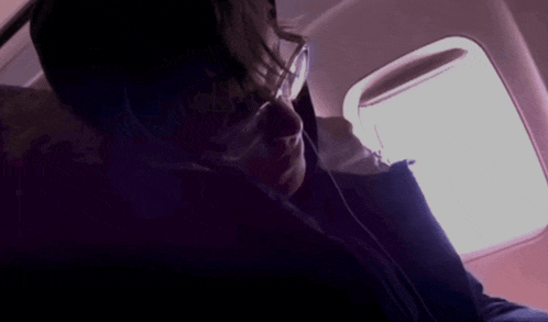 a man wearing glasses looks out a window on a plane