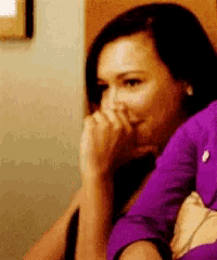 a woman in a purple shirt is covering her mouth with her hands .