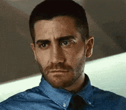 a man with a beard and a blue shirt and tie is looking at the camera .