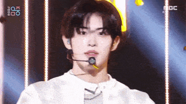 a young man is standing on a stage wearing a microphone and looking at the camera .