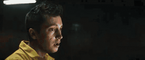 a man in a yellow shirt is standing in a dark room and looking at something .