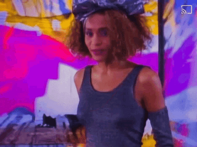 a woman wearing a gray tank top and a headband is standing in front of a painting .