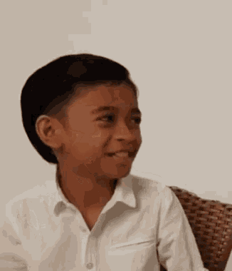 a young boy is sitting in a wicker chair and making a funny face .