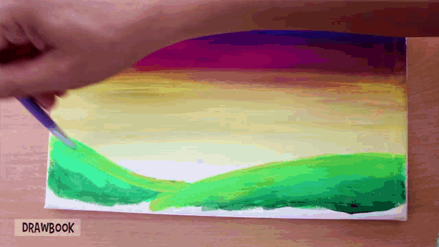 a person is painting a rainbow on a canvas with drawbook written underneath