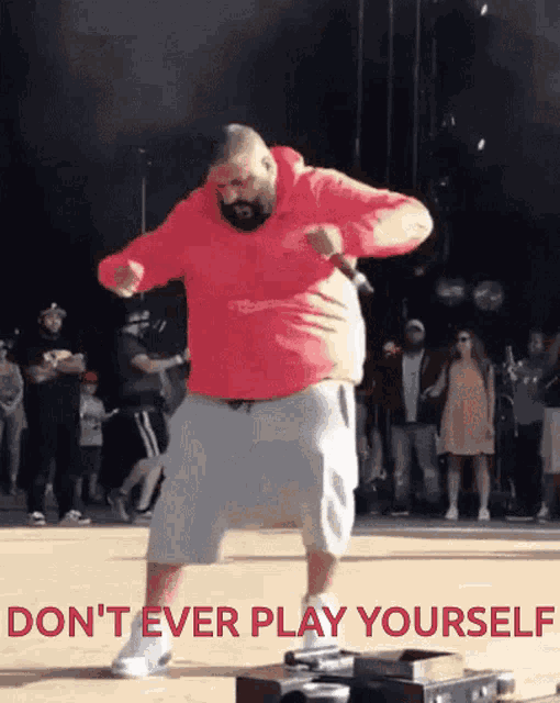 a man in a red hoodie is dancing on a stage with the words " do n't ever play yourself " behind him