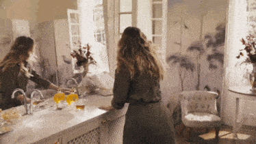 a woman standing in front of a bathroom sink looking at herself in the mirror