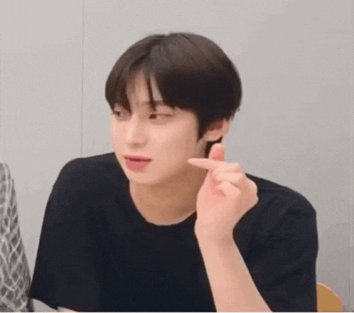 a young man in a black shirt is making a funny face while holding his finger to his mouth .