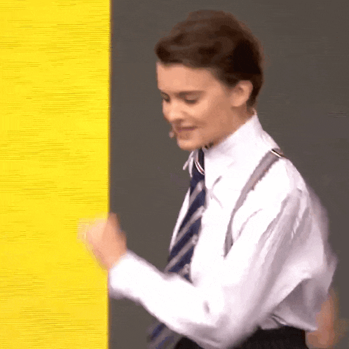 a young man in a white shirt and tie is standing next to a yellow wall .