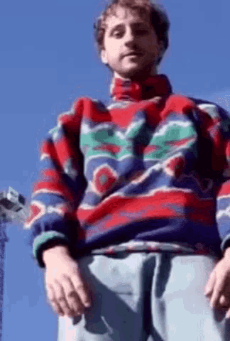 a man wearing a colorful sweater stands in front of a blue sky .
