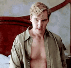 a shirtless man is standing in front of a bed looking at the camera