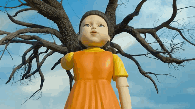 a doll in an orange dress stands in front of a tree without leaves