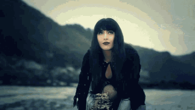a woman in a black jacket is kneeling in front of a lake