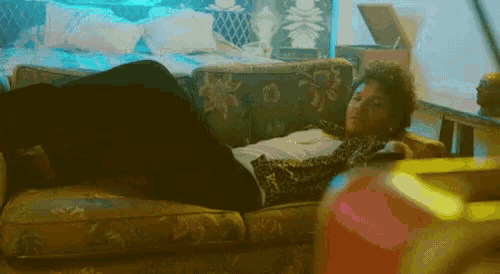 a man is laying on a couch with his legs crossed and watching tv