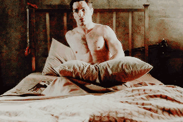 a shirtless man is laying on a bed with a pillow on top of him