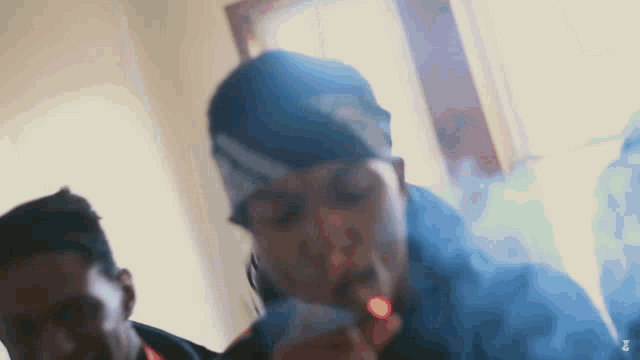 a man in a bandana is smoking a cigarette while another man looks on .