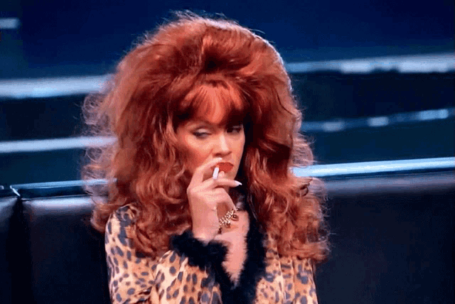 a woman with red hair is wearing a leopard print top and smoking a cigarette